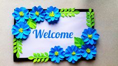 a welcome sign made out of paper with blue and green flowers on it's side