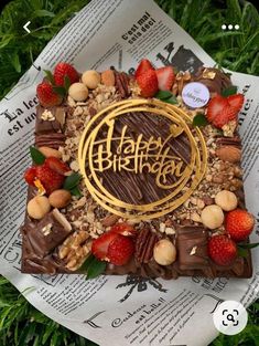 a birthday cake with nuts, chocolate and strawberries on it sitting in the grass