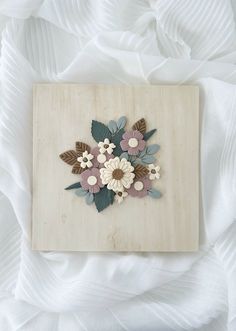 a wooden board with flowers and leaves cut out of it sitting on a white bed sheet