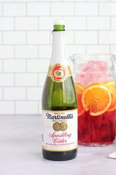 a bottle of sparkling cider next to a glass with ice and orange slices in it