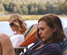 two women sitting on chairs next to each other in front of a body of water