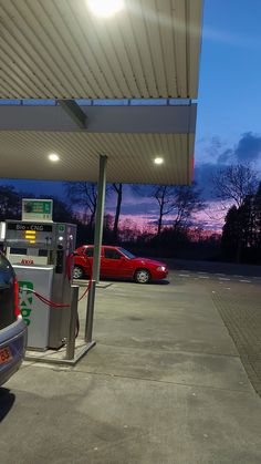 two cars parked at a gas station with the sun setting in the sky behind them