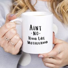 a woman holding a white coffee mug with the words,'antt no hood like motherhood '