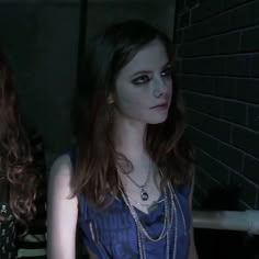 two young women standing next to each other in front of a brick wall and wearing necklaces