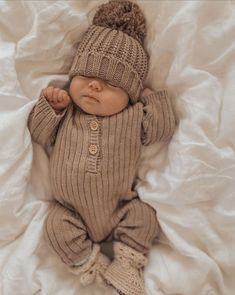 a baby wearing a knitted hat and sweater laying on top of a white sheet