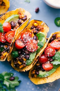 three tacos filled with black beans, tomatoes and cilantro on top of a blue plate