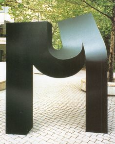 a large black sculpture sitting on top of a brick road next to a tree filled park