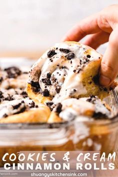 a person holding a cookie and cream cinnamon rolls in a glass baking dish with chocolate chips on top