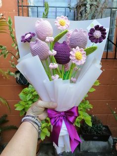 a person holding a bouquet of crocheted flowers in front of a brick wall