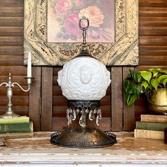 an ornate white lamp on top of a table next to books and a candle holder