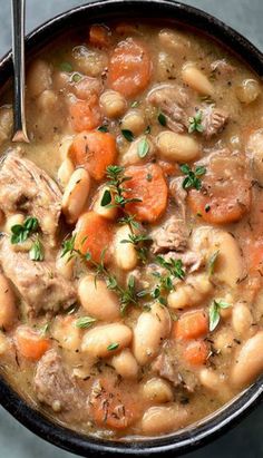 a bowl filled with meat and bean stew on top of a table next to a spoon