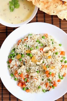 two plates with rice, peas and carrots next to some pita bread on a mat