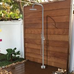 an outdoor shower in the backyard with rocks around it and a wooden fence behind it