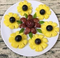 a white plate topped with yellow flowers and olives on top of a wooden table