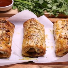 three pastries sitting on top of a cutting board next to a bowl of sauce