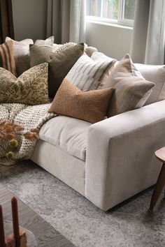 a couch with many pillows on top of it in front of a window and table