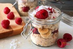 two jars filled with oatmeal and raspberries next to a cutting board