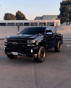 a black pickup truck parked in front of a fenced off parking lot next to a building