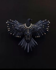 a black bird brooch with pearls on it's wings is shown in front of a dark background