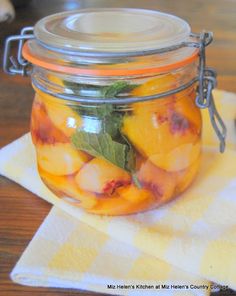 a glass jar filled with peaches and mint on top of a yellow checkered napkin