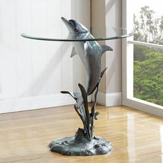 a glass table with dolphins on it in front of a window and wood flooring