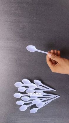 a hand holding a spoon over several white spoons