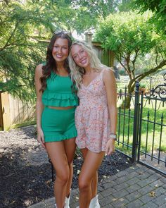 two beautiful young women standing next to each other in front of a fence and trees