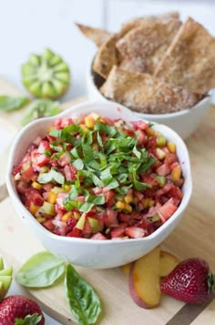 a white bowl filled with fruit and vegetables next to a baguette on a cutting board