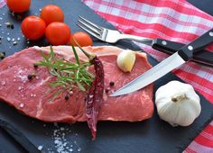 a piece of raw meat on a cutting board with garlic and tomatoes