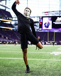 a man wearing a mask and black shorts standing on top of a field with his hands in the air