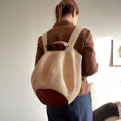 a woman standing in front of a white wall with a brown purse on her back