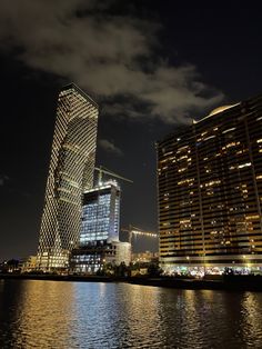 two tall buildings next to each other in the city at night with lights reflecting on the water