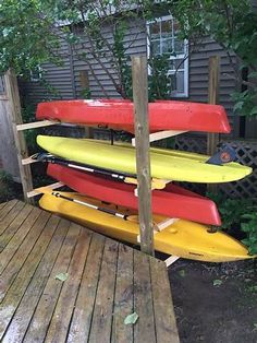 several kayaks are stacked on top of each other near a wooden deck in front of a house