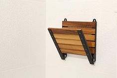 a wooden shelf mounted to the side of a white wall with black brackets on it