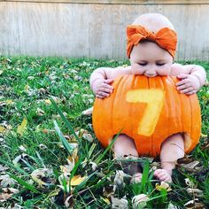 a baby sitting in the grass with a pumpkin shaped like a number seven on it's chest