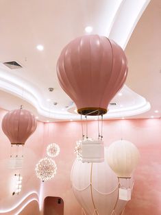 three hot air balloons suspended from the ceiling in a room with pink walls and ceilings