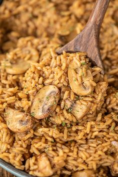 rice and mushrooms are being stirred with a wooden spoon