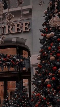 a large christmas tree sitting in front of a building with ornaments hanging from it's sides