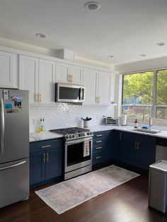 a kitchen with blue cabinets and stainless steel appliances in the center, along with an area rug on the floor