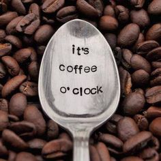 a spoon with the words it's coffee o'clock written on it in front of some coffee beans