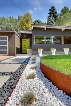 a modern house with grass and rocks in the front yard, as well as two large planters on each side