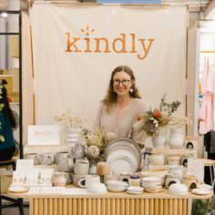 a woman standing behind a table with plates and vases on it's sides