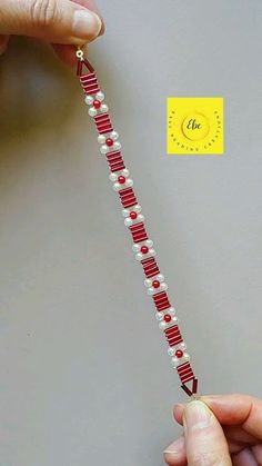 a person is holding a red and white beaded necklace on a string with a yellow tag attached to it