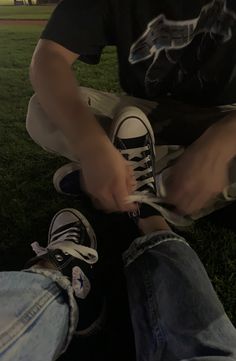 two people sitting on the grass tying their shoes with white laces and black sneakers