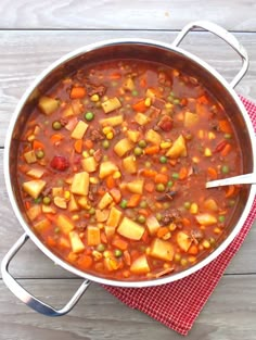 a pot filled with stew on top of a red cloth next to a wooden table