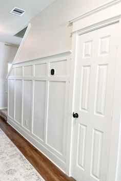 an empty room with white paneling and wood floors in the background, there is a carpet on the floor next to the door