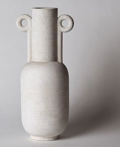 a white vase sitting on top of a table next to a gray wall and floor