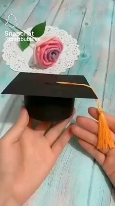 a hand holding a graduation cap with a rose on it