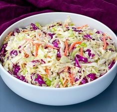 a white bowl filled with coleslaw on top of a purple table cloth next to a fork