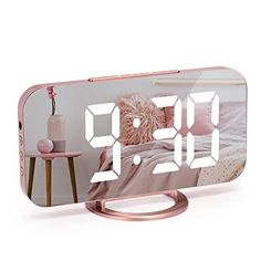 the alarm clock is on display in front of a white wall and pink bedding